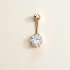Gold flower belly button ring with a clear gemstone on a beige background