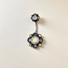Belly button ring with floral design and gemstones on a beige background