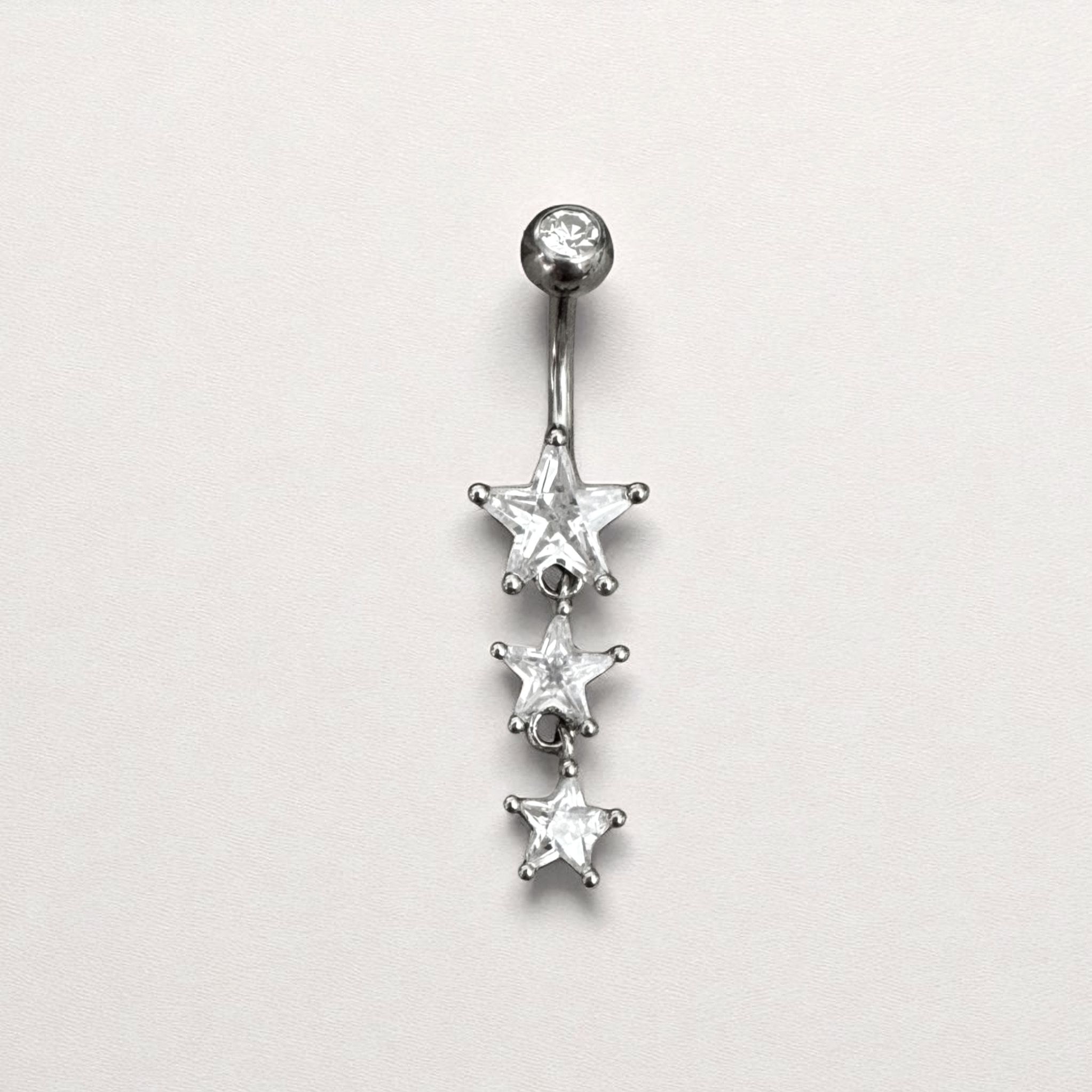 Silver belly button ring with three star-shaped gemstones on a light gray background