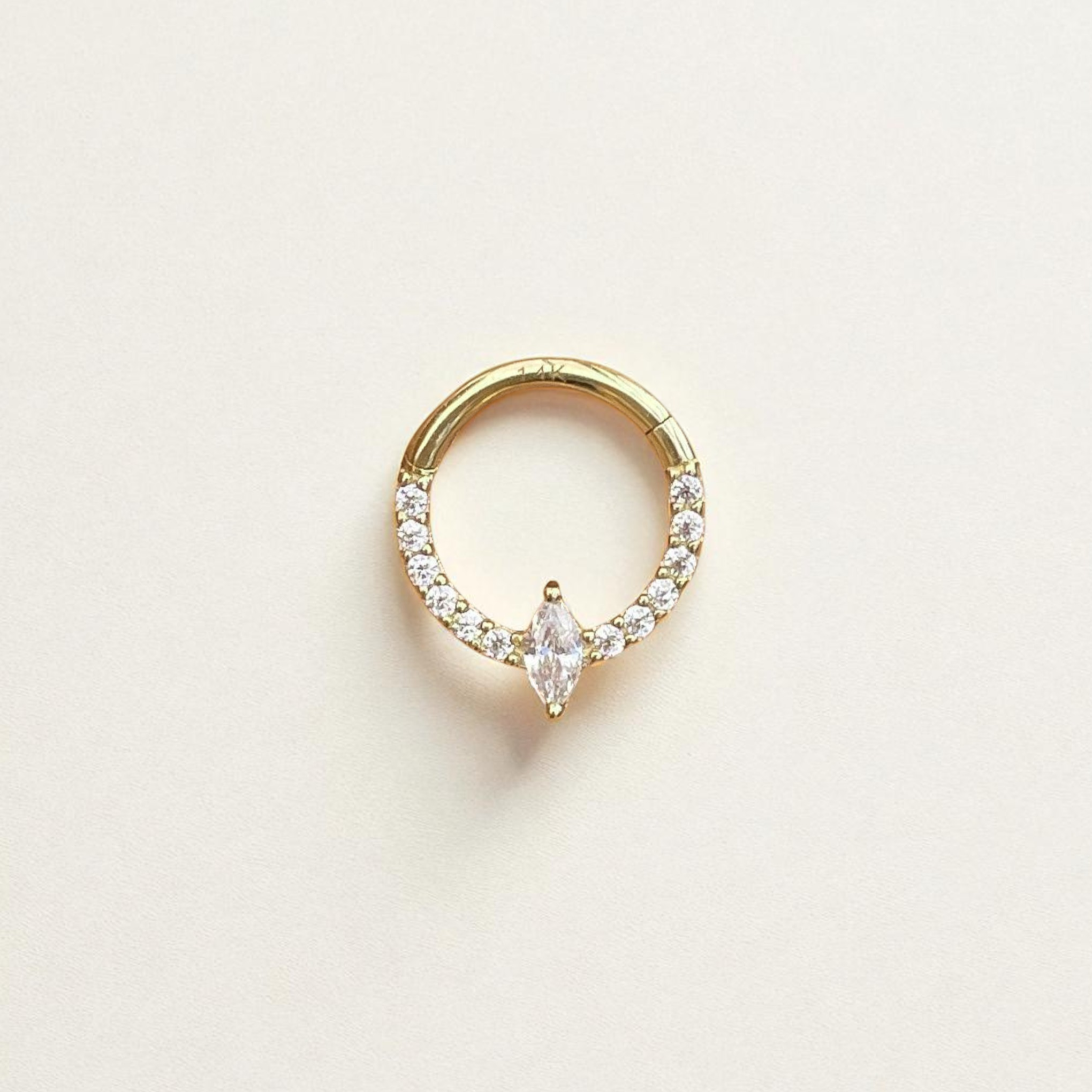 Gold daith earring with clear gemstones on a light beige background