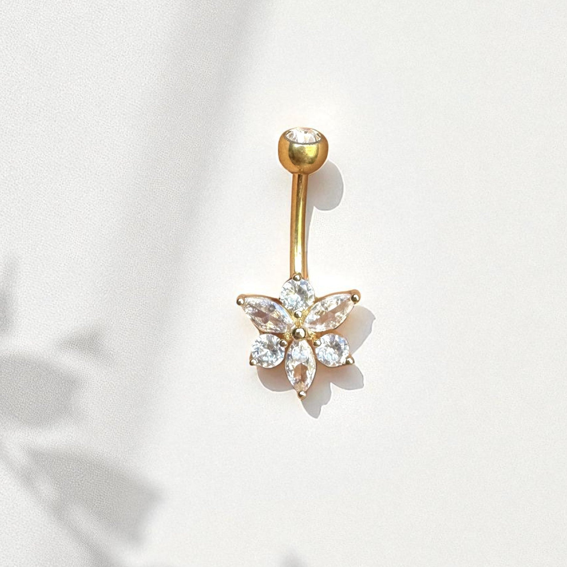 Gold belly button ring with floral design and clear gemstones on a white background