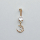 Gold belly button ring with a clear gemstone and moon design on a light gray background