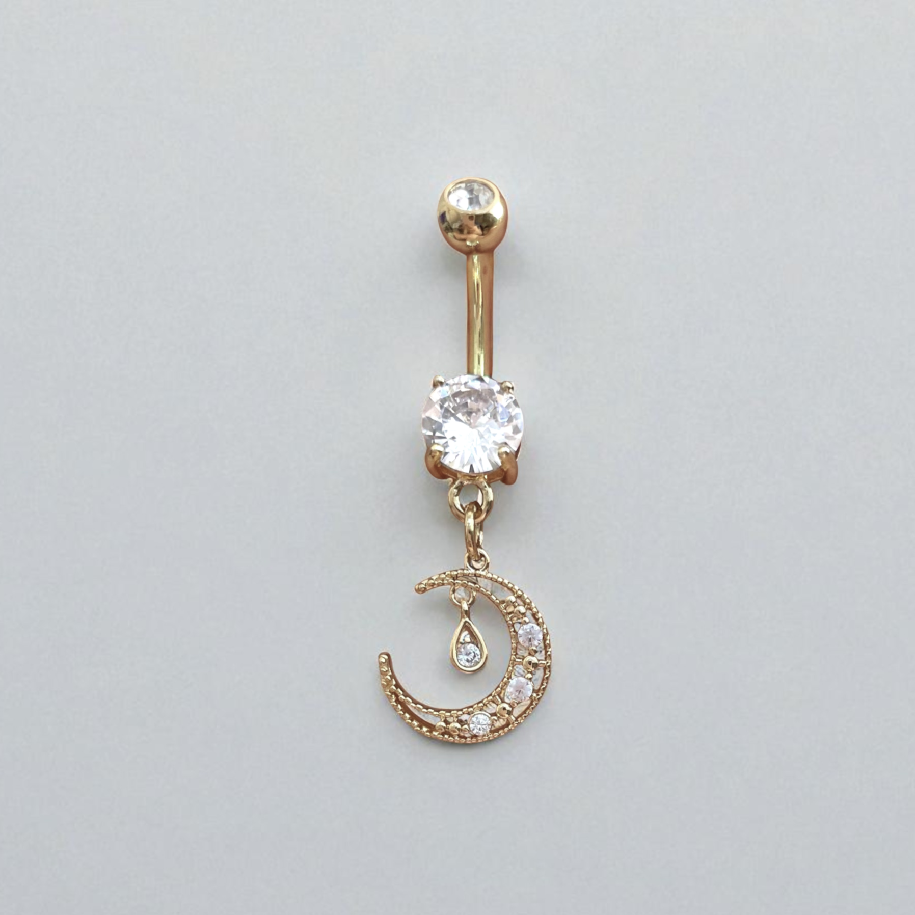Gold belly button ring with a clear gemstone and moon design on a light gray background