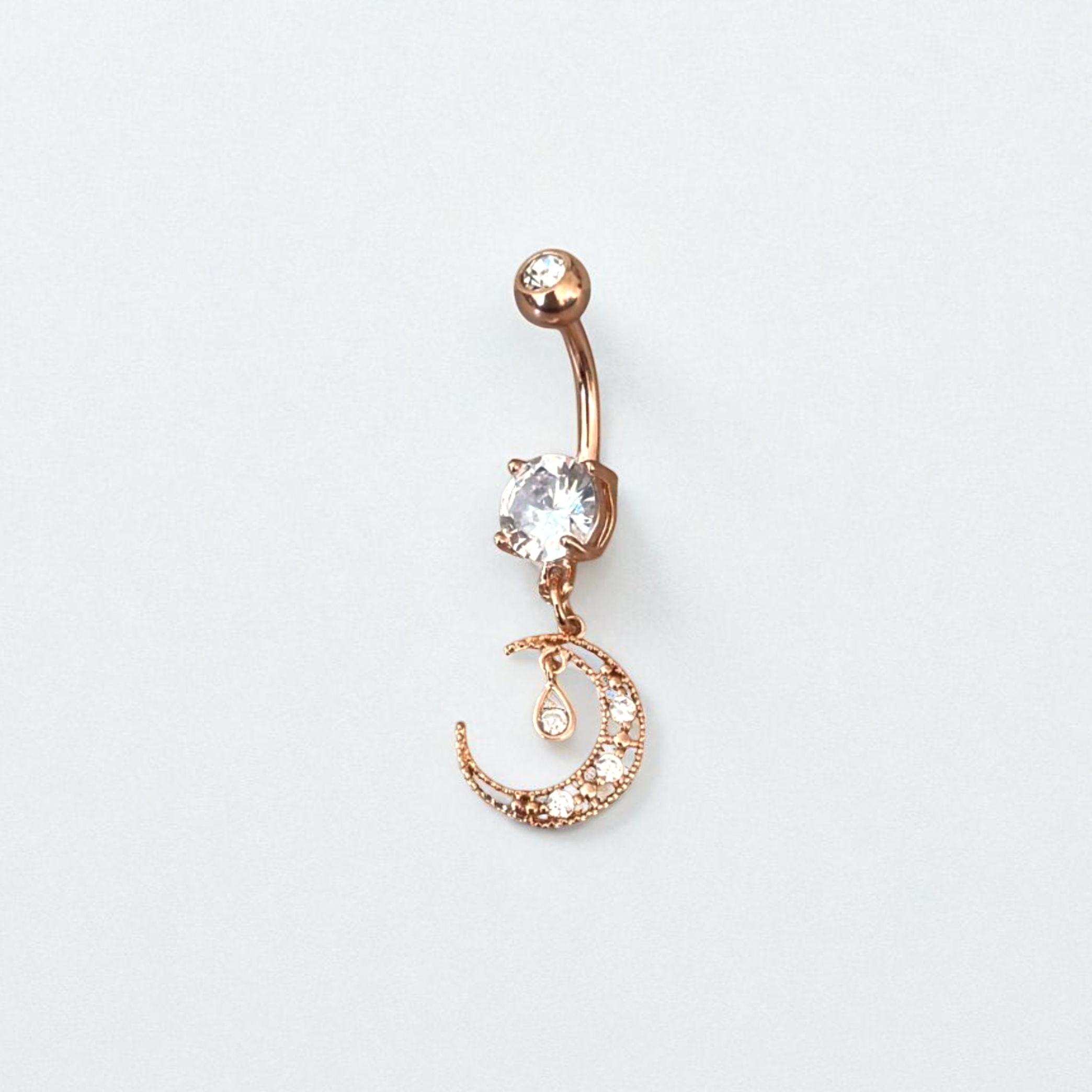 Rose gold belly button ring with a clear gemstone on a light gray background