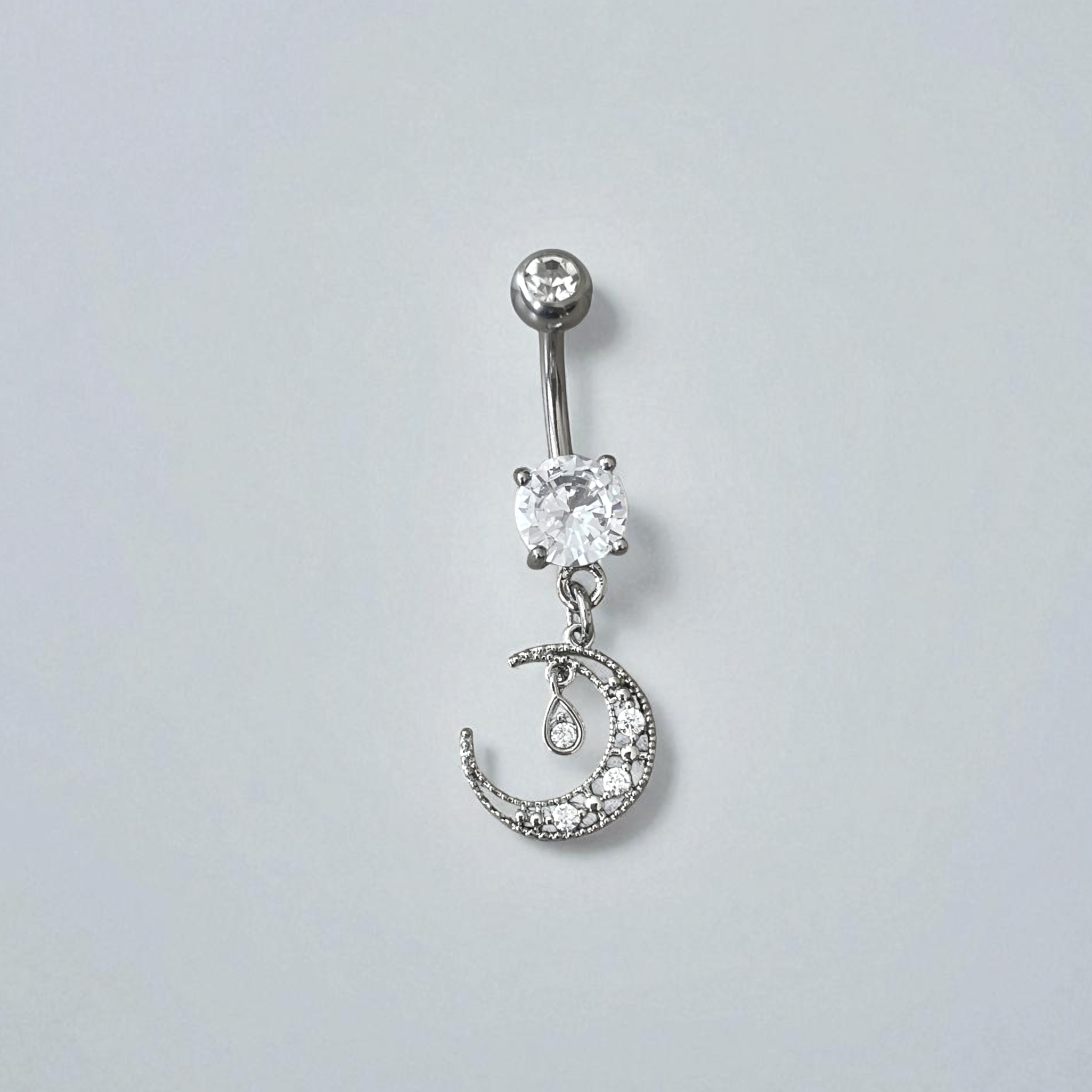 Silver belly button ring with clear gemstones on a light gray background