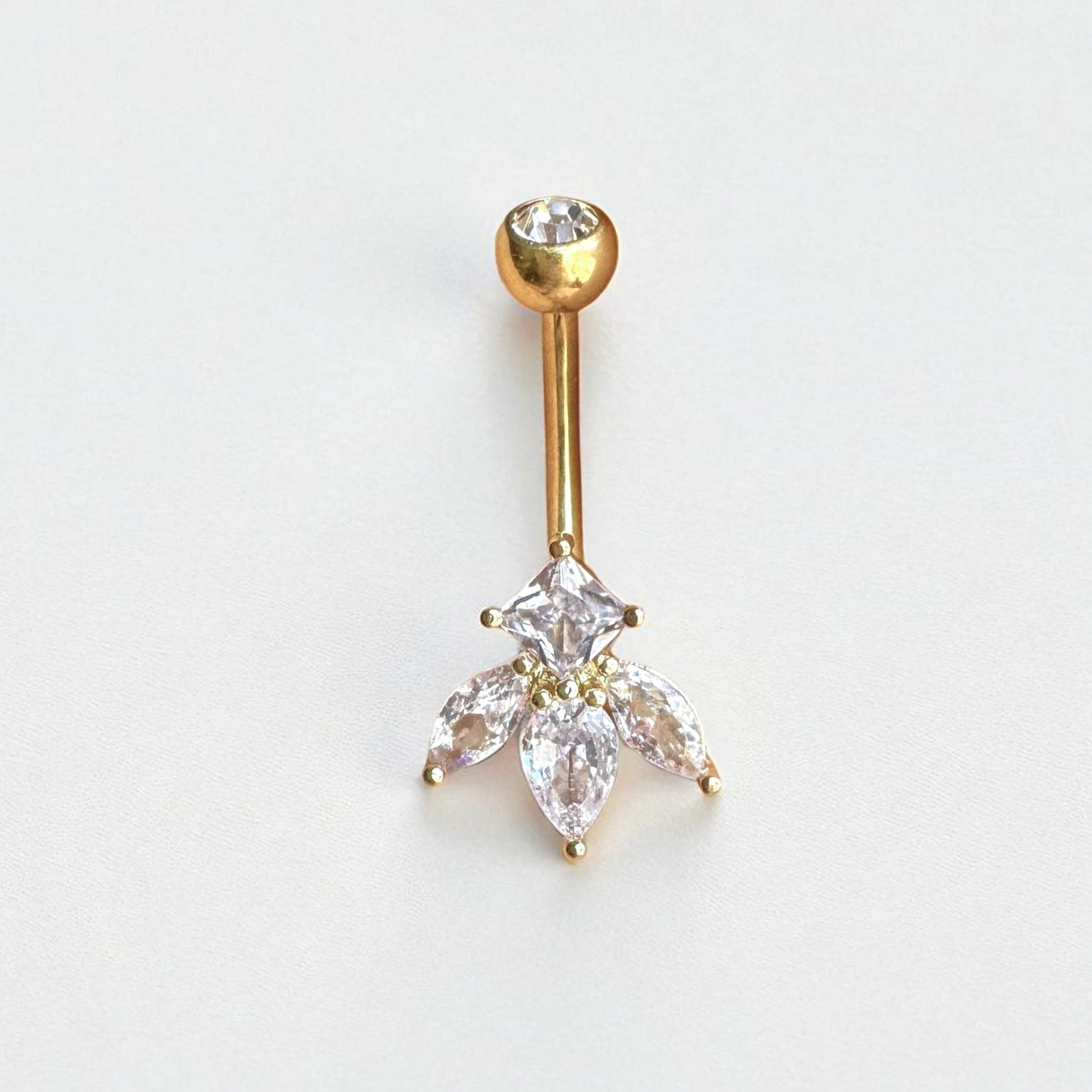 Gold belly button ring with clear gemstones on a light gray background