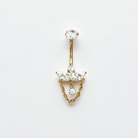 Gold belly button ring with clear gemstones and a dangly chain on a light gray background