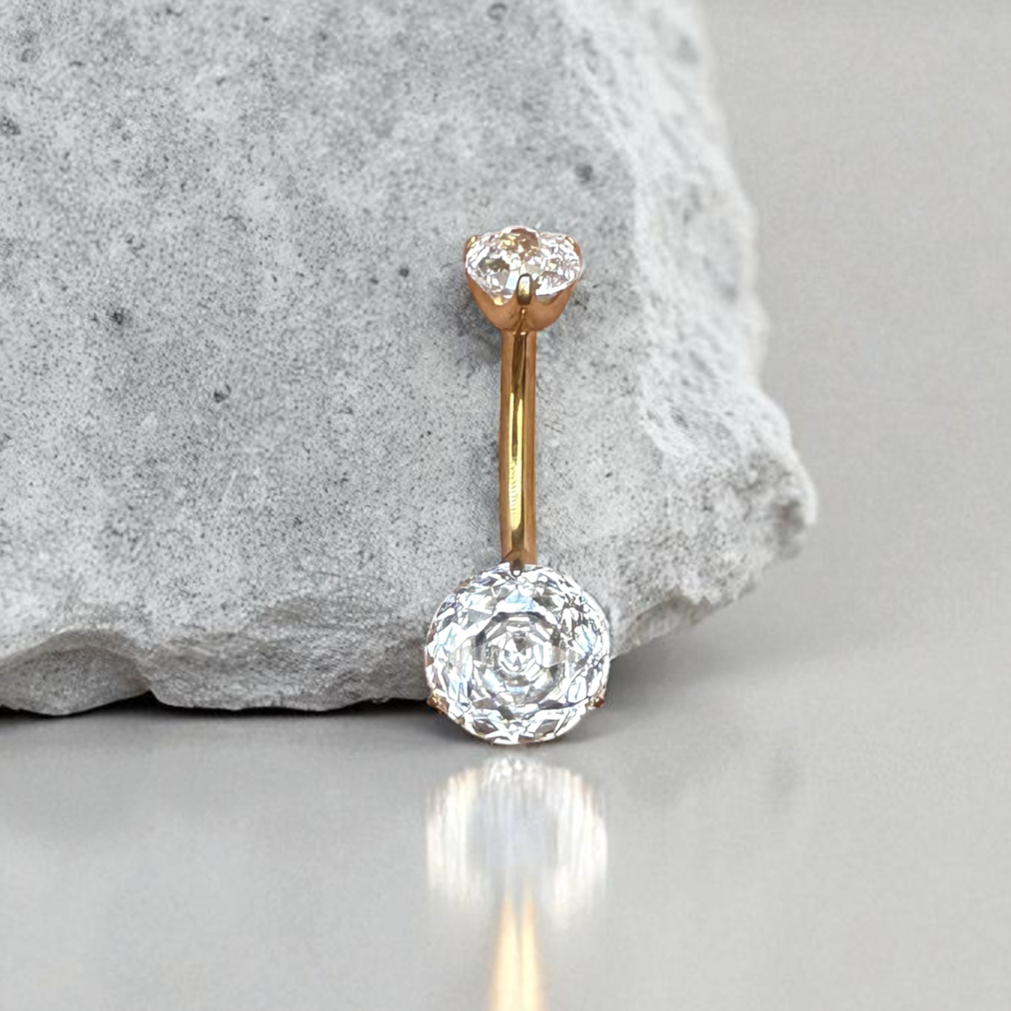 Gold belly button ring with clear gemstone on a gray surface