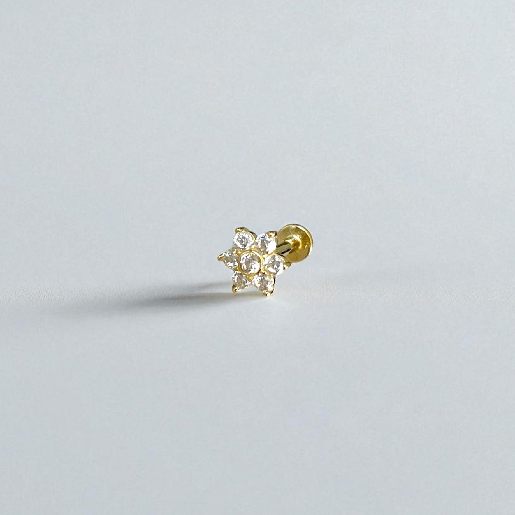 Gold flower flat back earring with clear gemstones on a light gray background