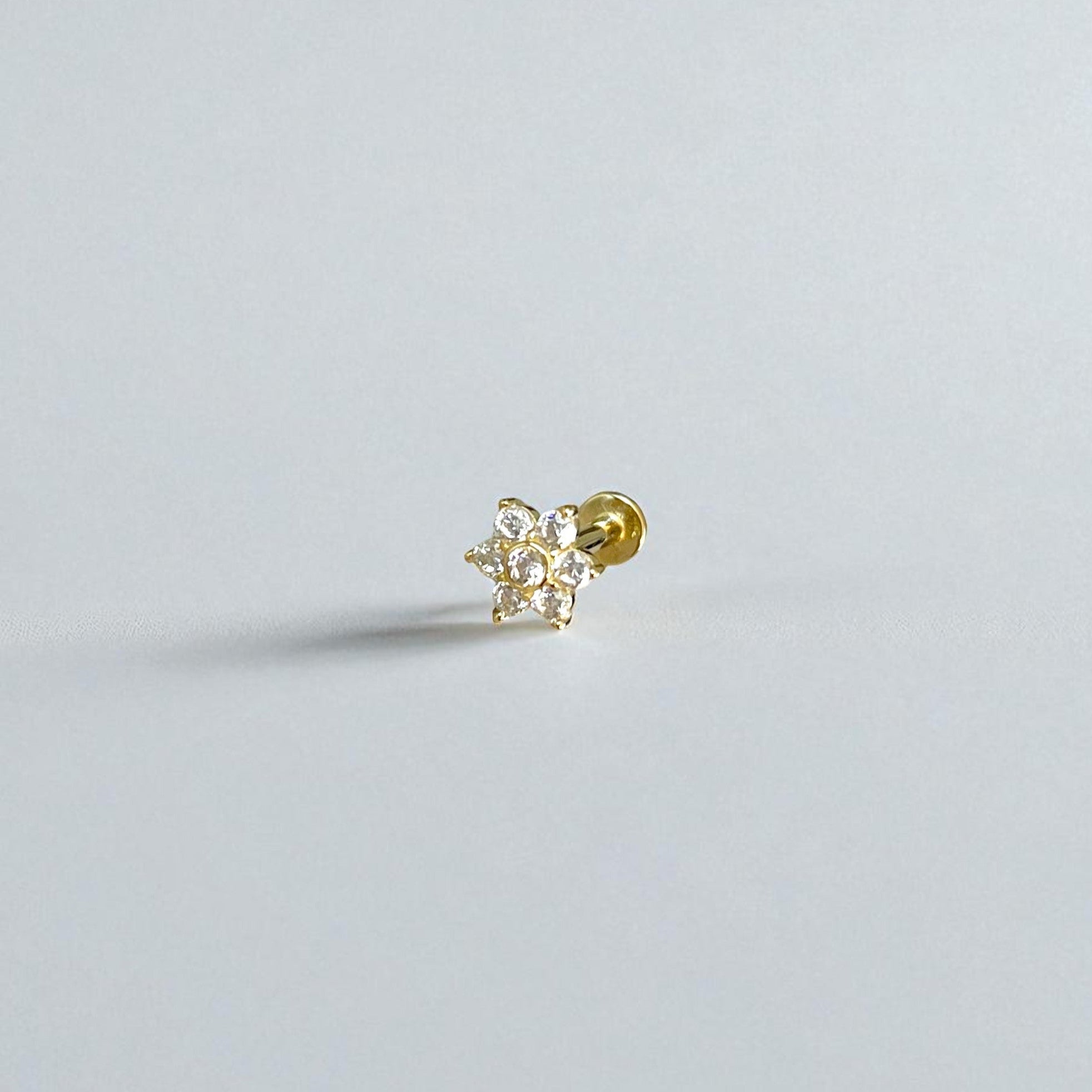 Gold flower flat back earring with clear gemstones on a light gray background