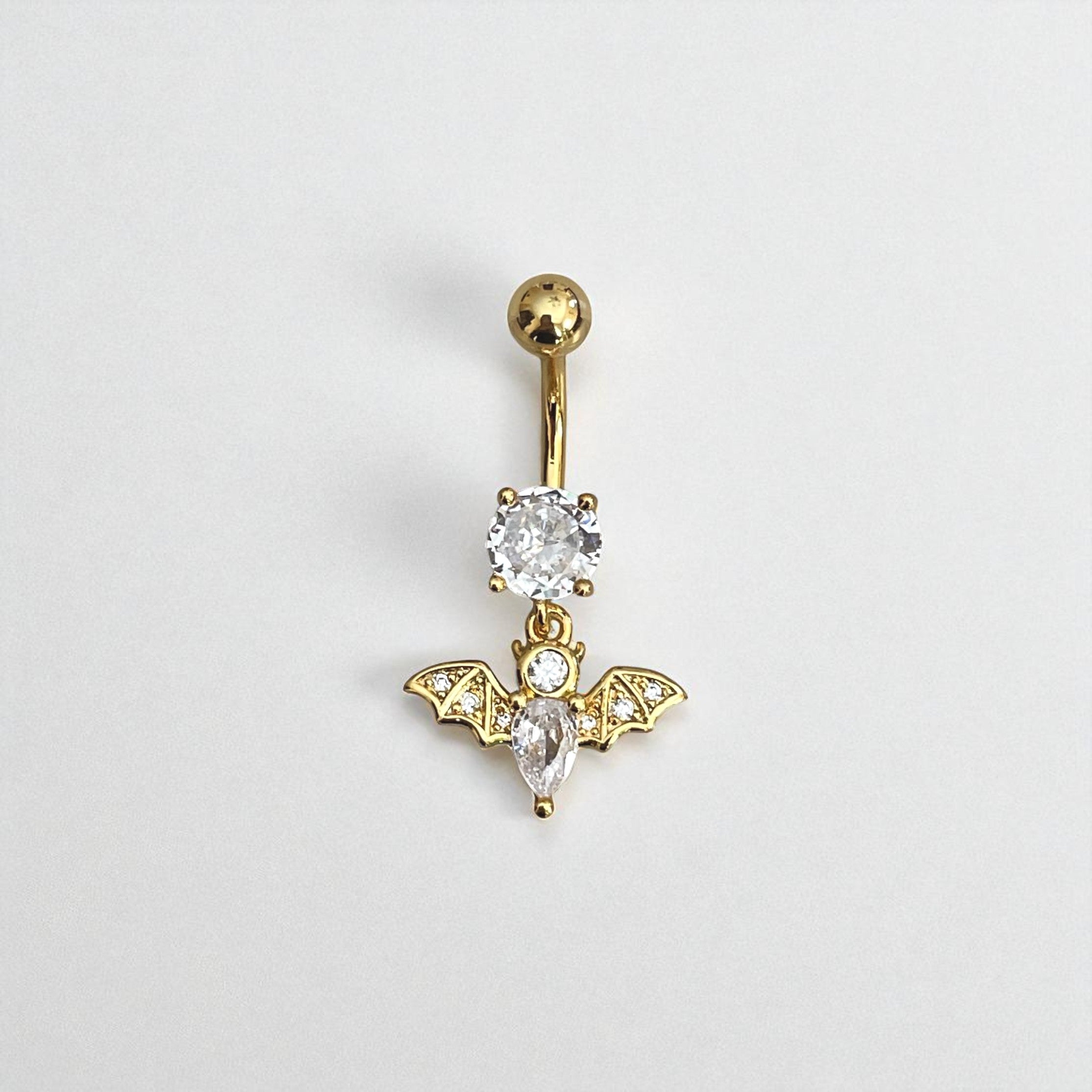 Gold belly button ring with bat design and clear gemstones on a light gray background