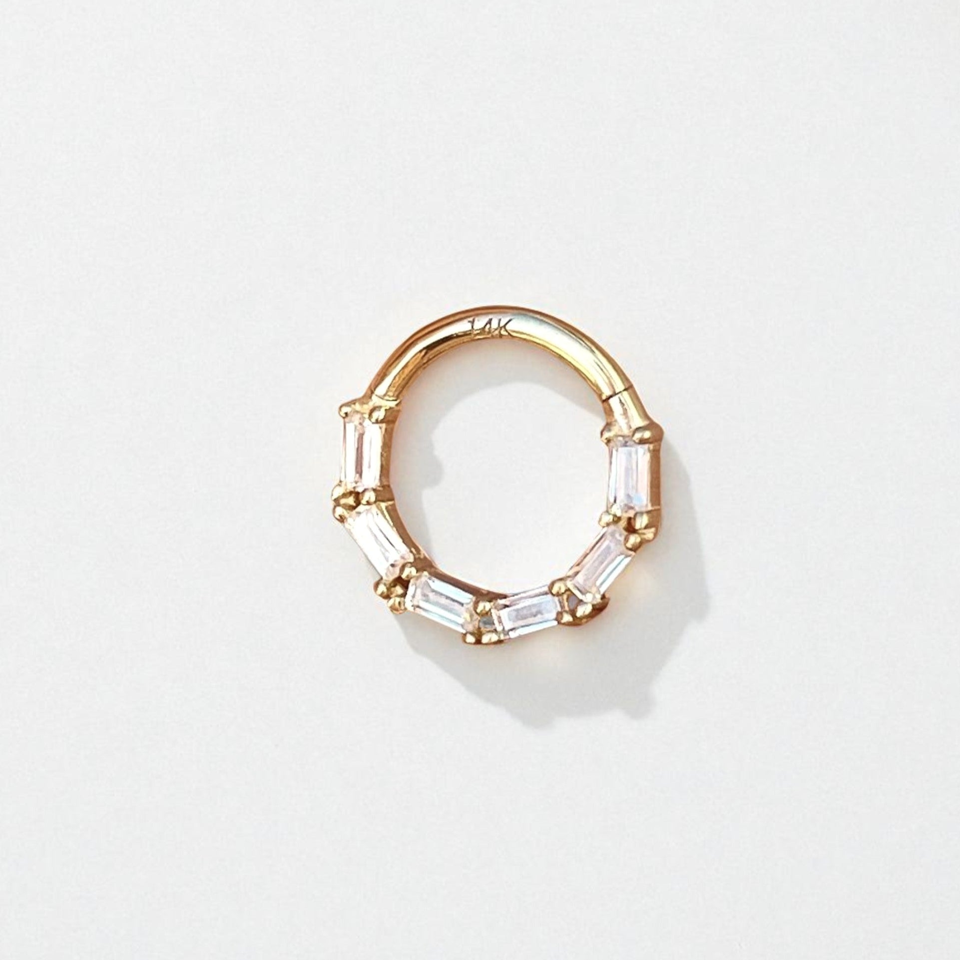 Gold hoop daith earring with clear baguette shaped gemstones on a light gray background