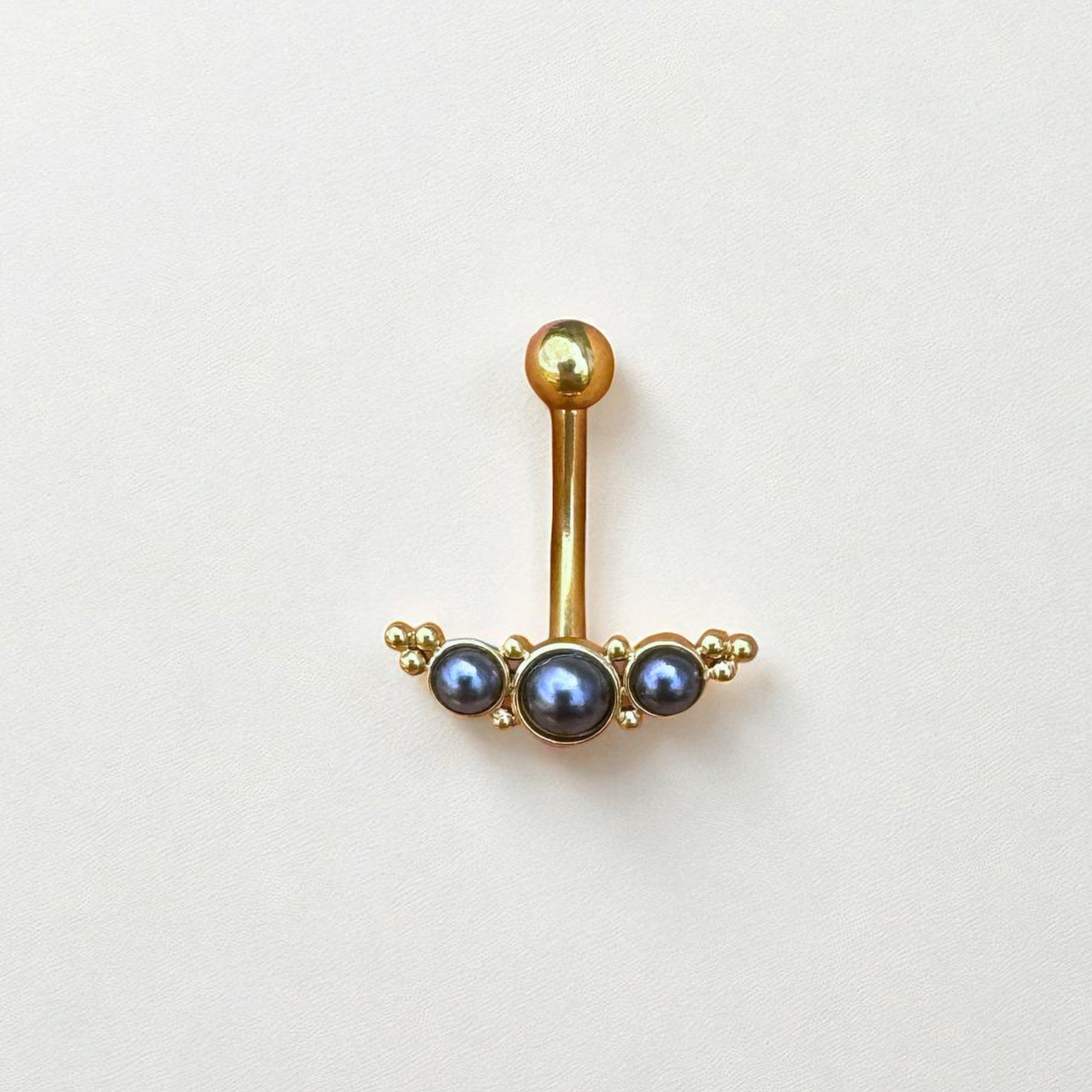Gold belly button ring with three dark pearls on a light gray background