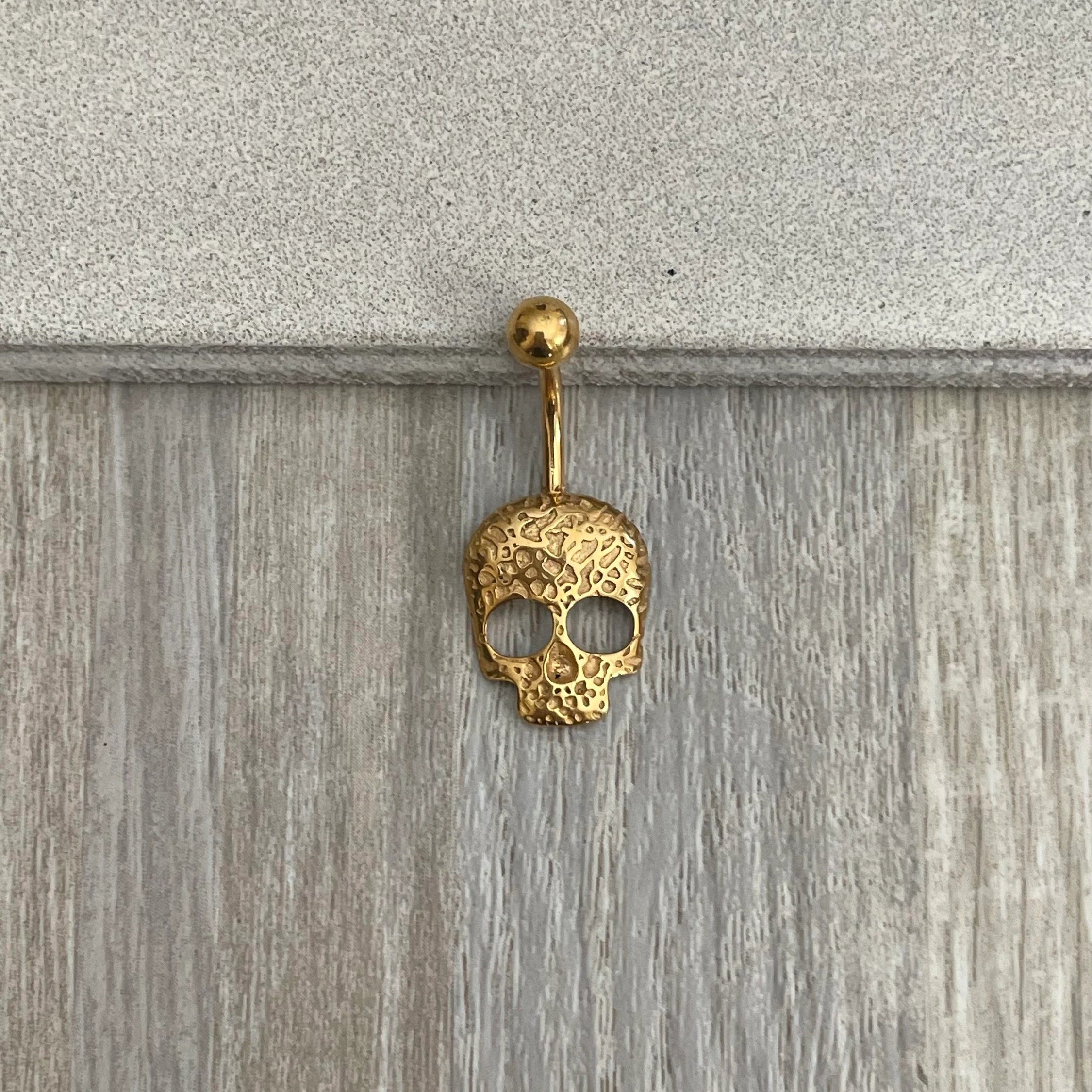 Gold skull-shaped earring on a wooden surface