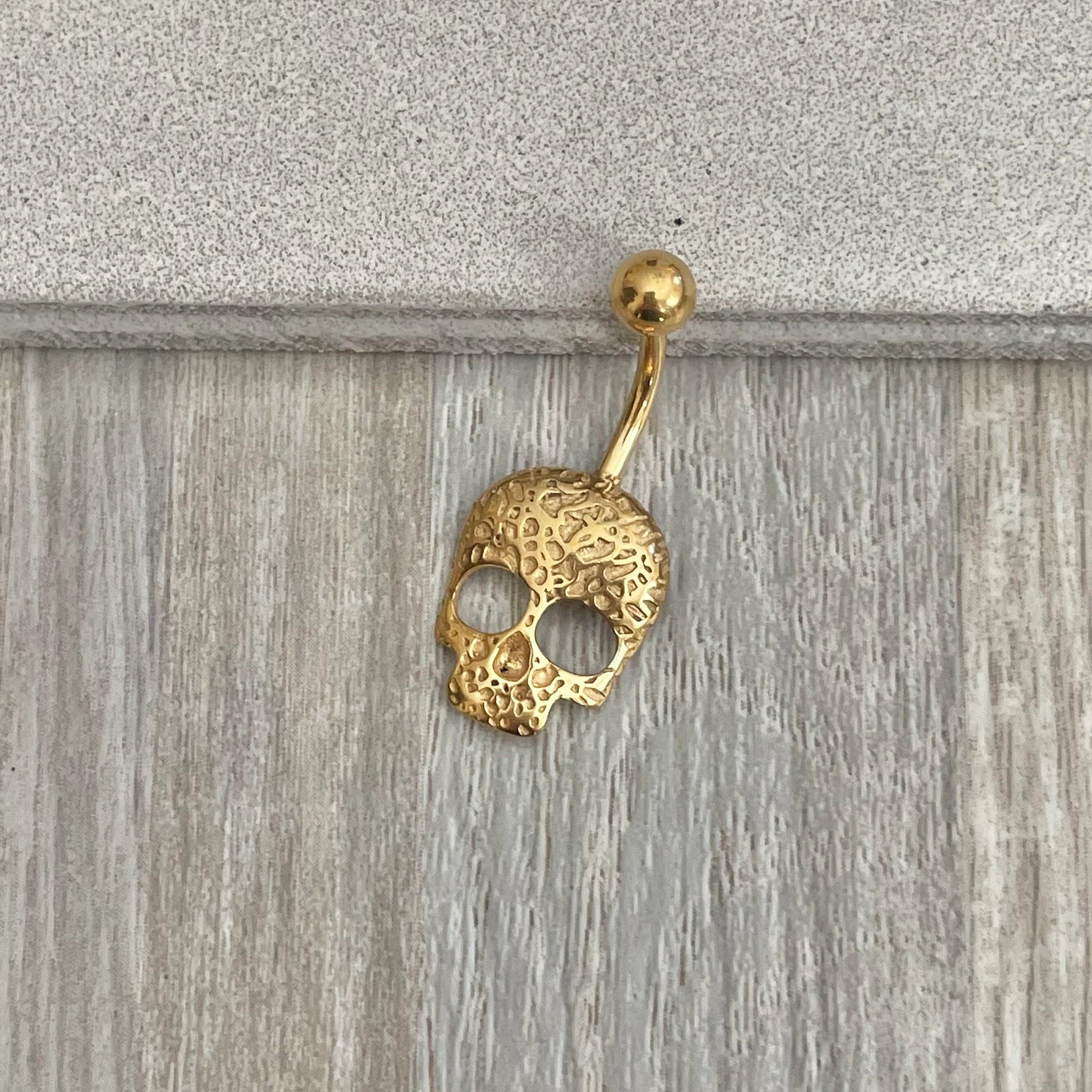 Gold skull-shaped belly button ring on a wooden surface