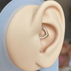 Close-up of an ear wearing a gold earring with clear stones on a blurred background