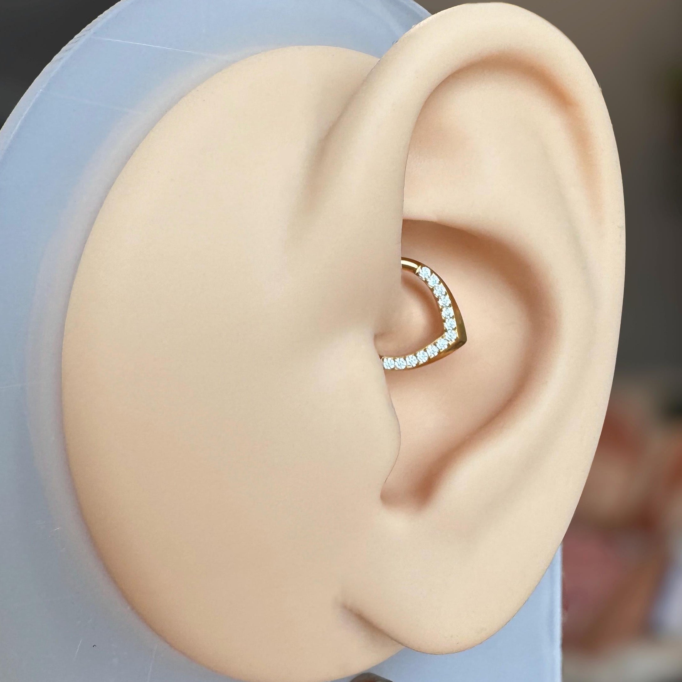 Close-up of an ear wearing a gold earring with clear stones on a blurred background